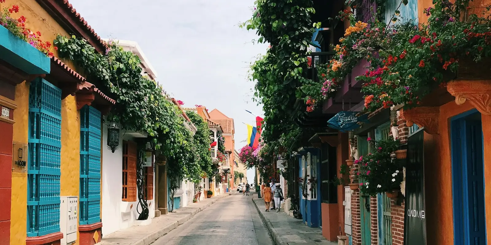A flower-draped street in Cartagena's old walled city, Colombian flag hanging over the lane ahead